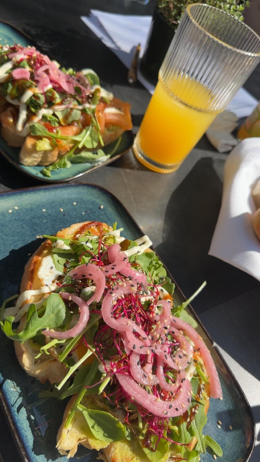 Frühstück in der Sonne: Sauerteigbrote mit Lachs, Avocado, Rucola, eingelegten Zwiebeln und Sesam, dazu ein Glas Orangensaft