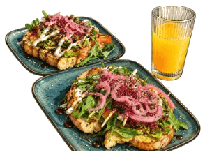 Zwei Avocado-Brote mit Rucola und eingelegten Zwiebeln, dazu ein Glas Orangensaft